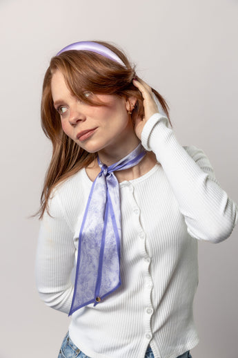 Woman wearing a white shirt and a light purple headband with a matching scarf.